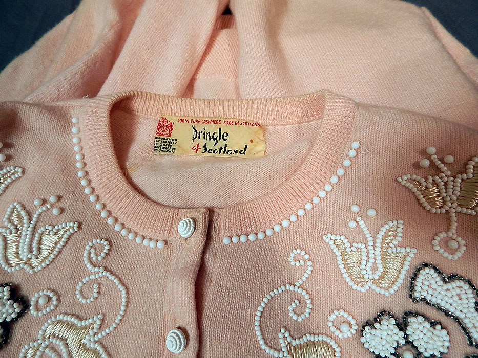 Vintage Pringle of Scotland Pink Cashmere White Beaded Cardigan Sweater
This beautiful beaded cardigan sweater has a ribbed fitted scalloped waistband, cuffs, collar, long full sleeves, unlined and white buttons down the front for closure. 