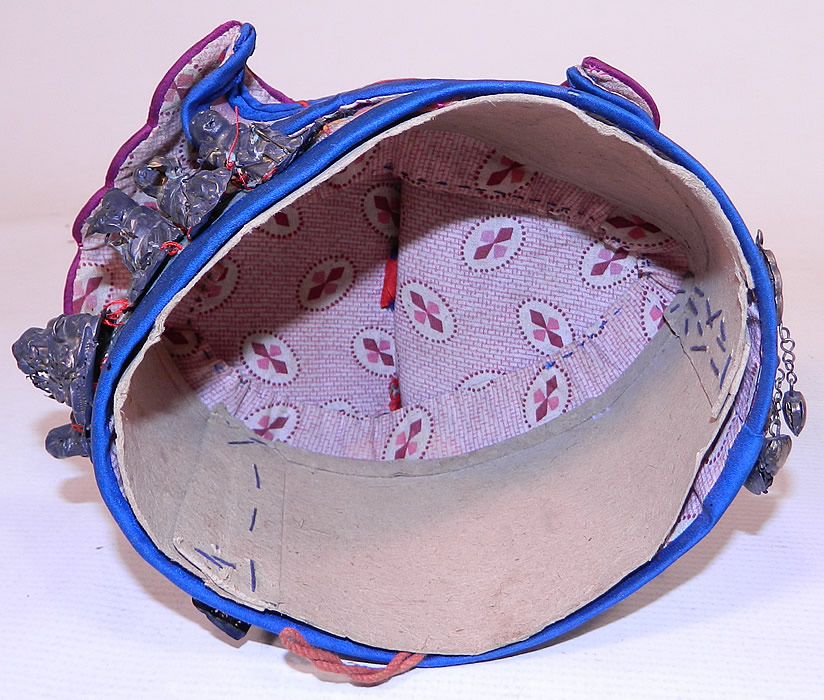 Antique Chinese Child Infant Silk Embroidered Silver Immortals Charm Wind Hat
This child's wind hat has a round pill box shape, with applique fabric layers and is fully lined in a purple and white cotton calico print fabric, with cardboard ring inside to keep its shape.