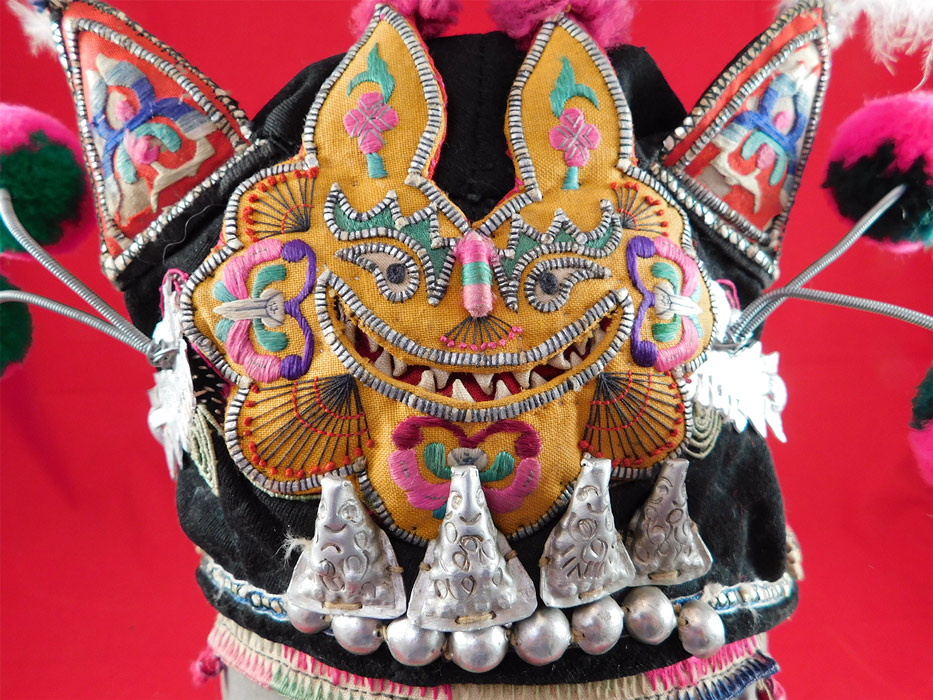 Antique Chinese Bai Miao Minority Childrens Festival Embroidered Tiger Wind Hat
This whimsical children's hat has a yellow detailed raised padded smiling grinning tiger face on the front, with red cat ears trimmed in white feathers on the top, colorful pompom whiskers attached with springs.