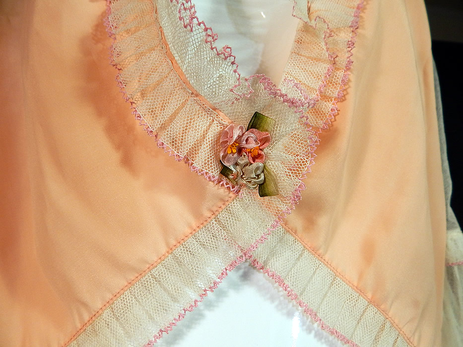 Vintage Pink Silk White Ruffle Rosette Trim Lingerie Boudoir Bed Jacket
This lovely lingerie boudoir bed jacket blouse top has a short crop cutaway style shorter in the front, longer in the back, with sheer 3/4 length sleeves, ruffle cuffs, an open front with a single snap closure hidden underneath the rosette trim at the waist and is sheer, unlined.