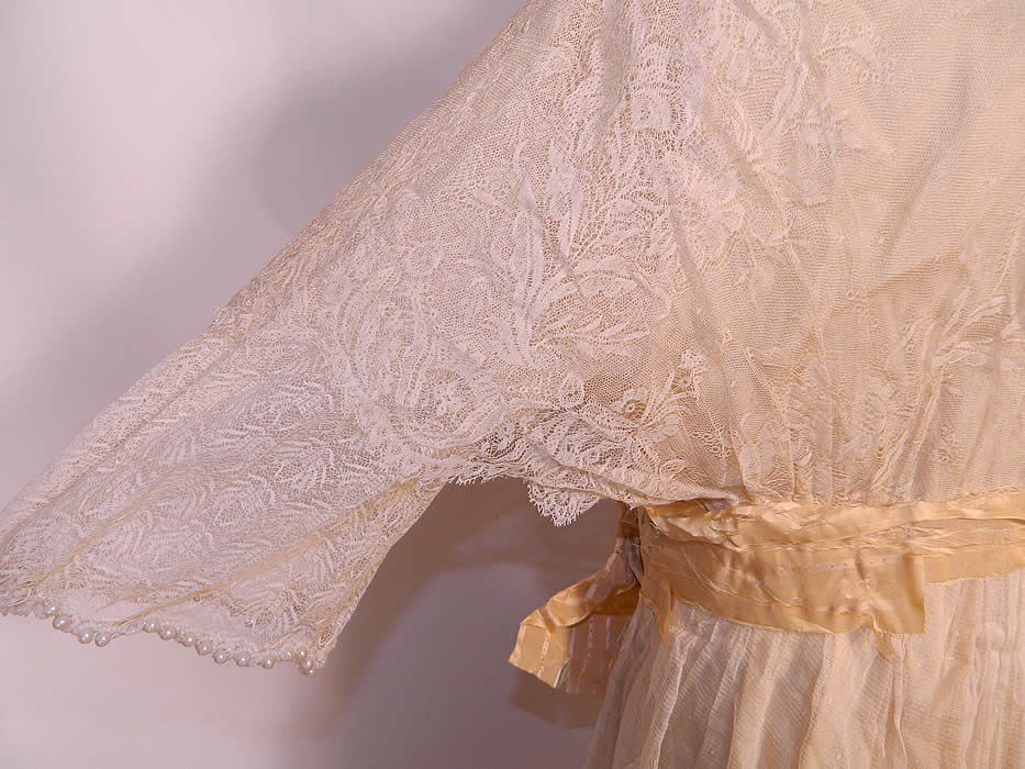 Edwardian Titanic Cream Silk Lace Pearl Beaded Wedding Gown Dress. This beautiful bridal wedding gown dress has a layered, tiered style, with sheer lace insert necklines, 3/4 length sleeves, an attached ribbon belted sash, long floor length wrap style skirt with side drape and snap closures. 