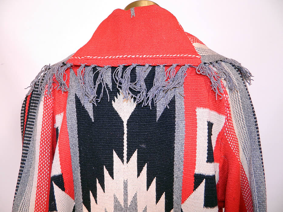 Antique Chimayo Blanket Red Wool Hand Woven Long Duster Coat. This beautiful blanket long floor length duster style coat is loose fitting, has a gray fringe trim edged wide lapel shawl collar, two large patch pockets with bottom fringe trim, long full sleeves with rolled cuffs top fringe trim and an open front with no closure. 