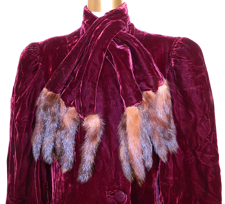 Vintage Burgundy Silk Velvet Mink Fur Tails Scarf Evening Coat Winter Jacket. This elegant evening coat is a long floor length, with a fitted style, gathered shoulders, broad shoulder padding, long full bishop sleeves with fitted cuffs, fully lined, an attached neck collar scarf wrap and velvet button closure.