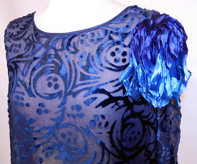 Art Deco Vintage Blue Silk Burnout Voided Velvet Drop Waist Flapper Dress. This fabulous flapper style loose fitting drop waist dress has long full sleeves, with fitted cuffs, a velvet varying shades of blue floral cut strips trim on the shoulder, blue silk panels hanging down the back and on the bottom skirt with smocking gathers along the hips. It is sheer and unlined. The dress measures 44 inches long, with 42 inch hips, a 36 inch waist, 38 inch bust and 23 inch long sleeves.