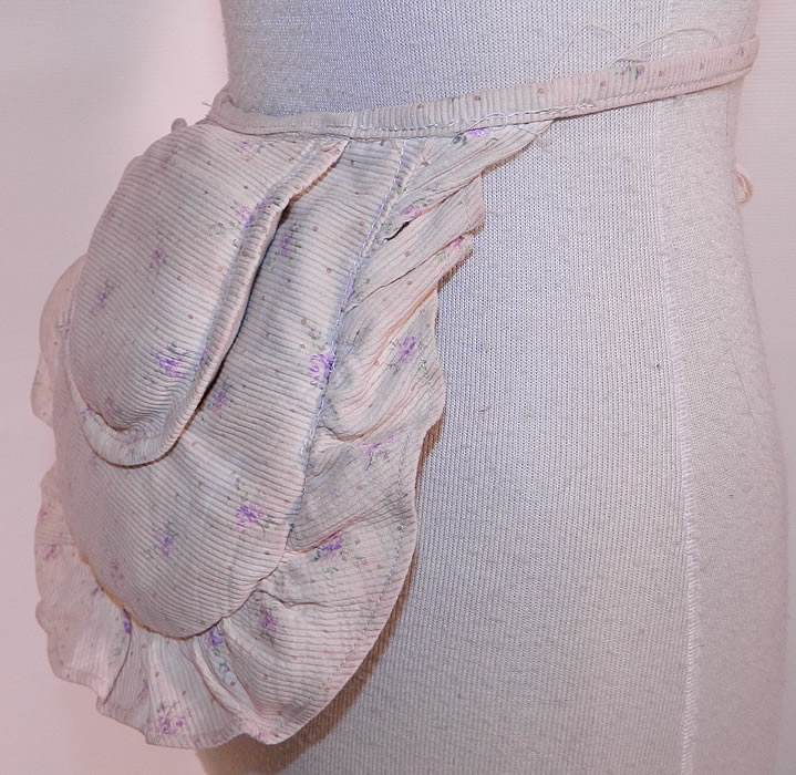 Victorian White Cotton Pique Purple Violet Polka Print Crinolette Bustle Pad Support. This pretty pad is created in a puffed pillow crescent shape, with a layered double pad design and ruffle trim edging. There is a cotton cloth strap tie belt around the waist.