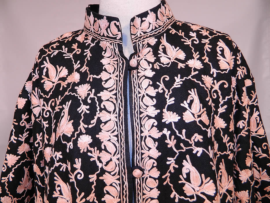 Vintage Black Wool Pink Chain Stitch Crewel Work Embroidery Ethnic Coat Jacket. The design work completely covers the entire coat. This exquisite ethnic Kashmiri Indian inspired loose fitting boxy coat jacket is a long floor length, with long full sleeves, an embroidered mandarin collar, round fabric buttons for closure down the front, side pockets and is fully lined.