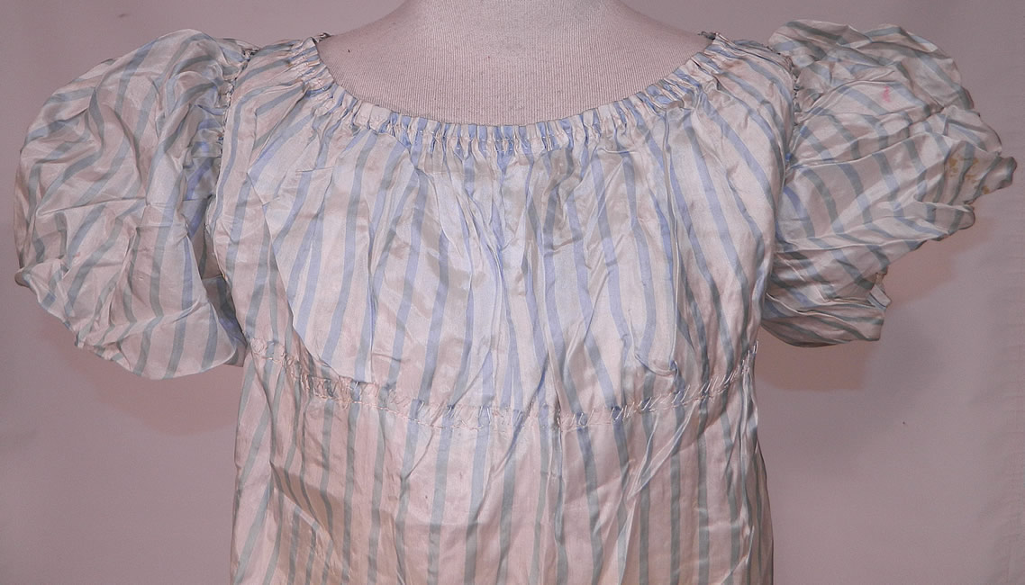 Antique Georgian Regency Era Blue & White Stripe Silk Puff Sleeve Girls Dress
It is hand stitched, made of a light periwinkle blue and white striped fine silk fabric. This gorgeous Georgian girls gown would have been worn by a young lady and has a high empire waist with gathered stitching which would have had drawstring closures around it and the neckline, puff balloon shape gigot sleeves and a ruffle bottom hem skirt. 