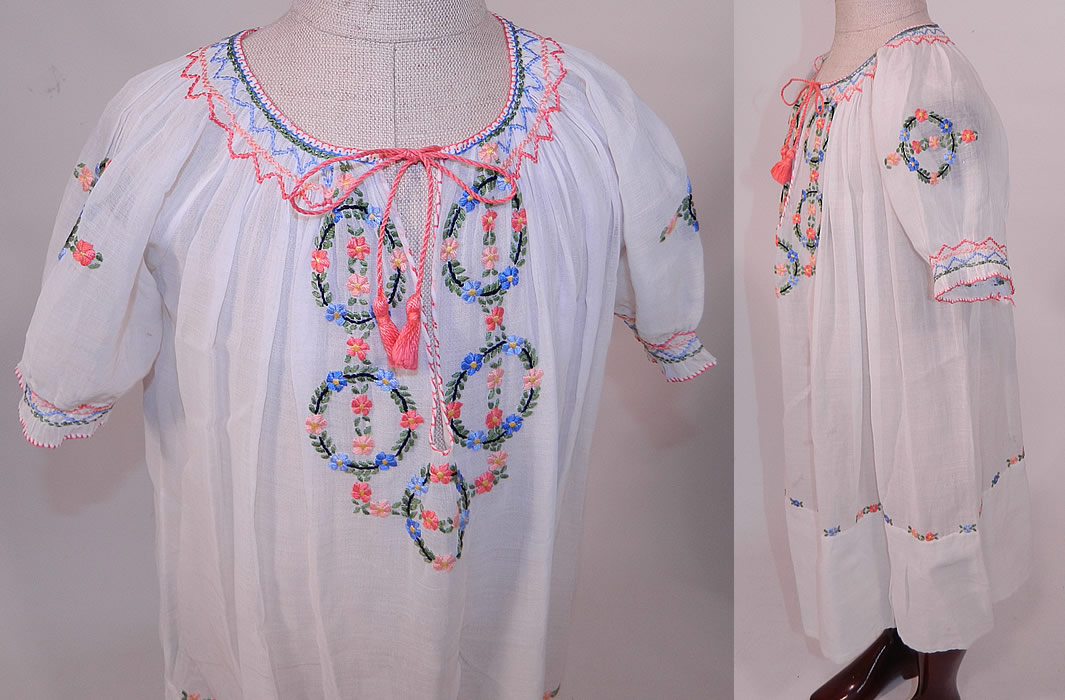 Vintage Childs White Cotton Colorful Embroidered Smocking Hungarian Peasant Dress
This pretty peasant style bohemian Hungarian little girls dress has a loose fitting shift style, with short sleeves, a drawstring front neckline, smocking around the neck, sleeve cuffs and is sheer, unlined.