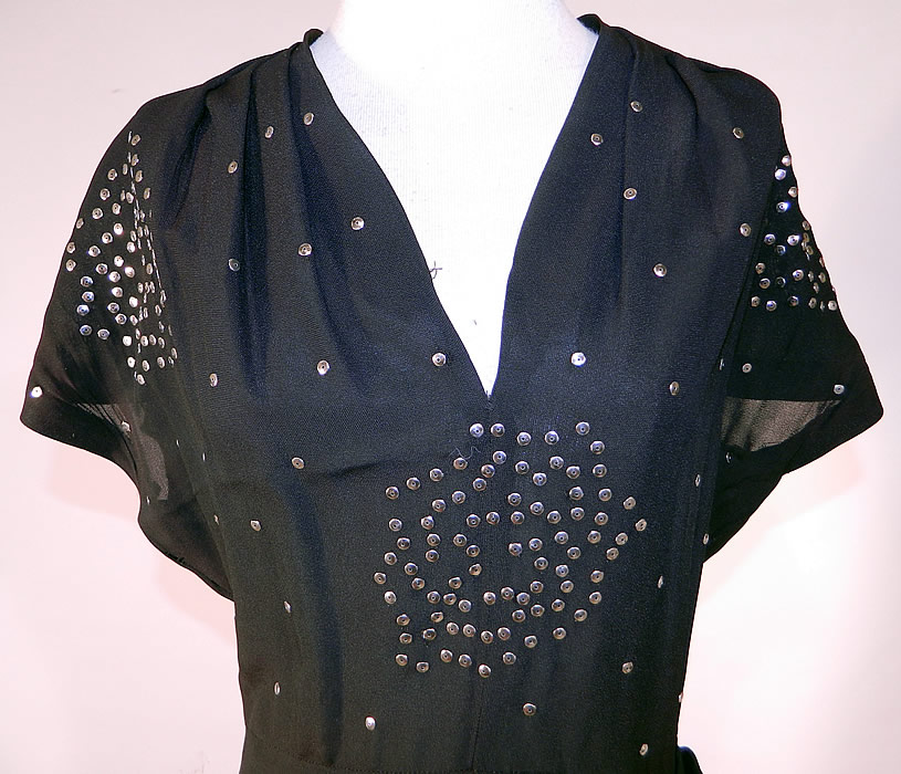 Vintage Black Silk Silver Metal Sequin Studded Beaded Cocktail Dress
This stunning studded cocktail dress has a V front neckline, short cap sleeves, a short mid length skirt with side hip drape gathering, a side zipper closure and is sheer, unlined.