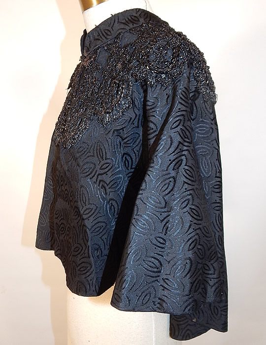 Victorian Black Silk Damask Brocade Jet Beaded Trim Mourning Cloak Cape
It is made of a black silk damask weave brocade fabric with a woven abstract leaf pattern design and black jet beaded trim appliques sewn around the neckline.