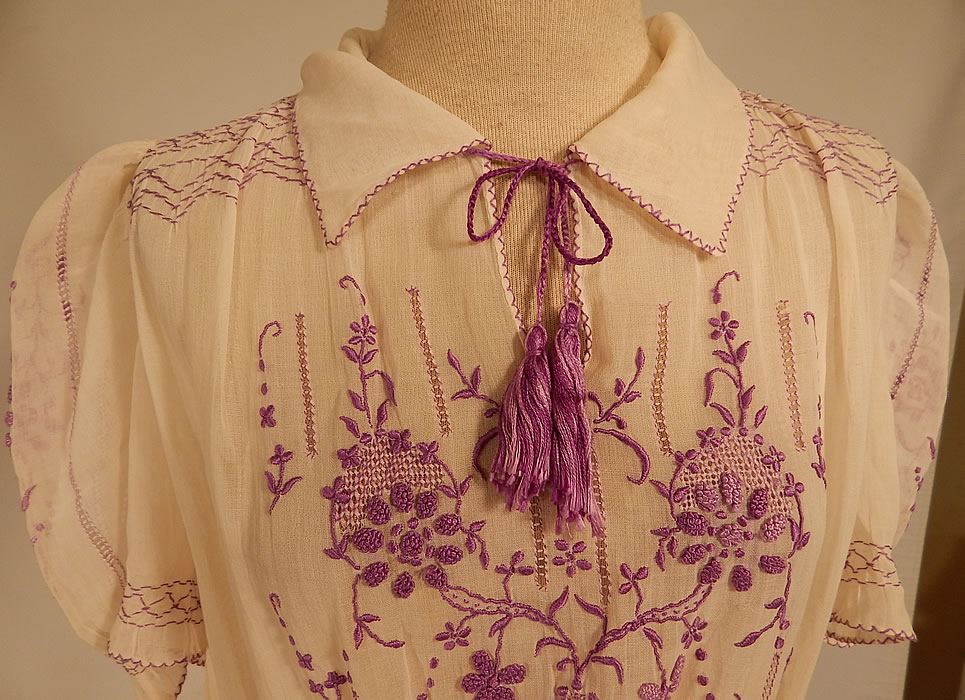 Vintage White Cotton Purple Embroidered Smocking Boho Peasant Drop Waist Dress
This pretty peasant style bohemian Hungarian Czech dress has a drop waist style, with smocking detail around the waist, shoulders with gathering, short puffy sleeves, a fold over collar, with tassel tie front neckline, side snap closures and is sheer, unlined. 