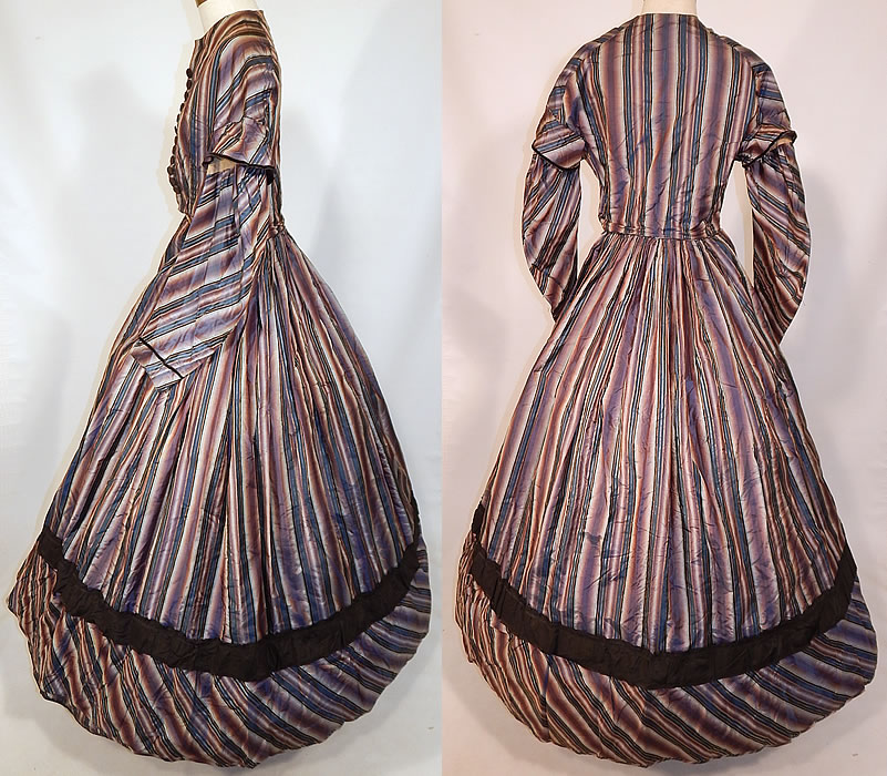 Victorian Civil War Era Purple & Blue Ombre Stripe Silk Hoop Skirt Gown Dress
This stunning striped dress has a long floor length full hoop skirt (hoop not included underneath), with attached fitted bodice top, long layered full sleeves, brown velvet trim, faux button trim with hidden hook closures underneath down the front, side skirt pockets with a bundle of extra dress fabric wrapped inside and is fully lined. 