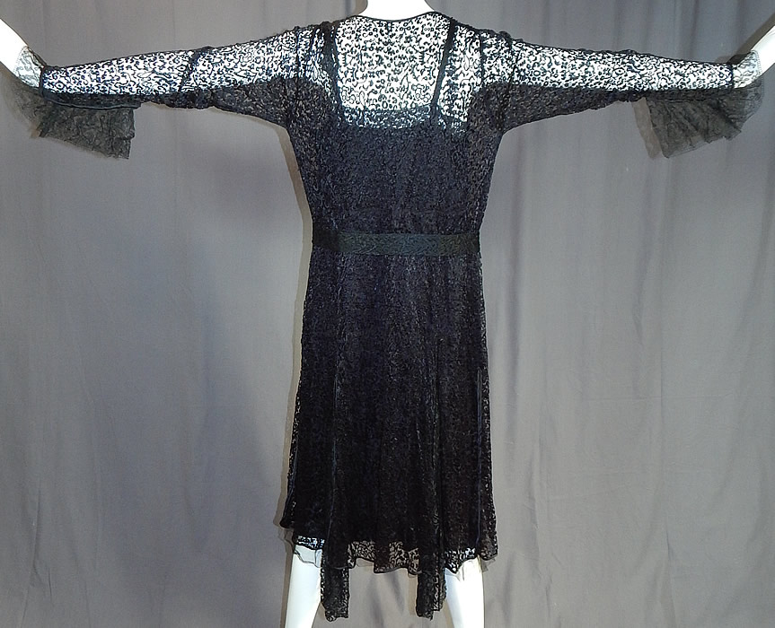 Vintage Art Deco Buckle Belted Black Silk & Chantilly Lace Flapper Dress
This fabulous flapper dress has an open front low V neckline, with black silk slip lining inside which has black Chantilly lace trim edging along the top and bottom, a lace belt with Art Deco style rhinestone buckle clasp at the waist, long tapered sleeveless with flared gauntlet cuffs, an uneven handkerchief skirt hemline and snap closures along the side of the slip.