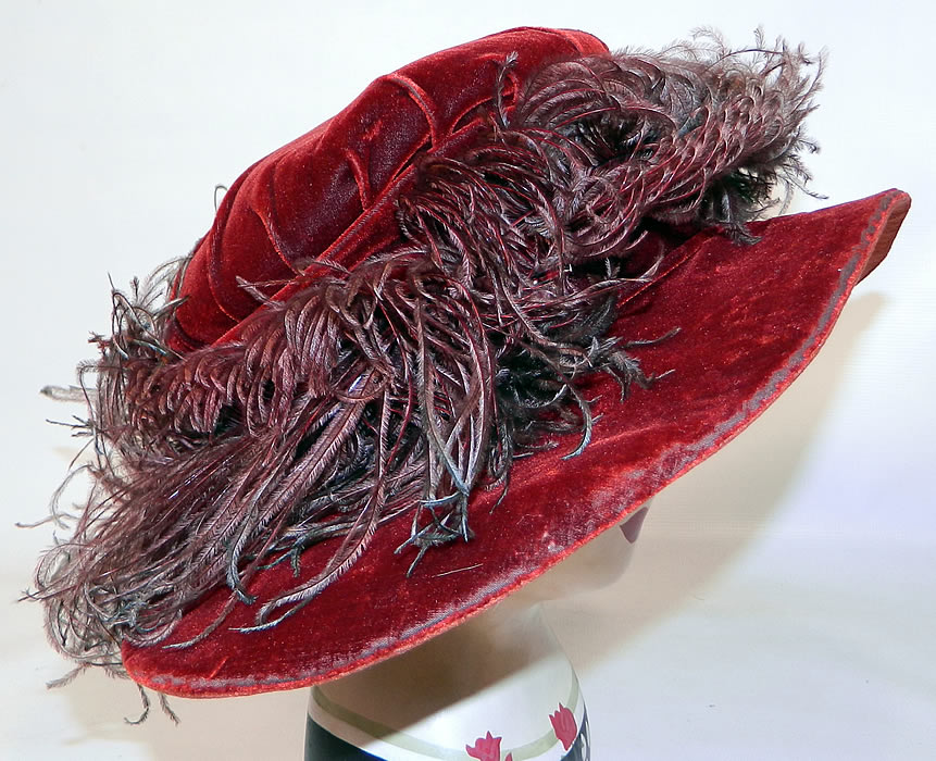 Vintage Fall Color Burgundy Red Velvet Feather Boa Trim Wide Brim Cloche Hat. The hat is made of a dark red burgundy wine color velvet fabric, with ombre color brown to green ostrich feather boa trim surrounding the crown. 