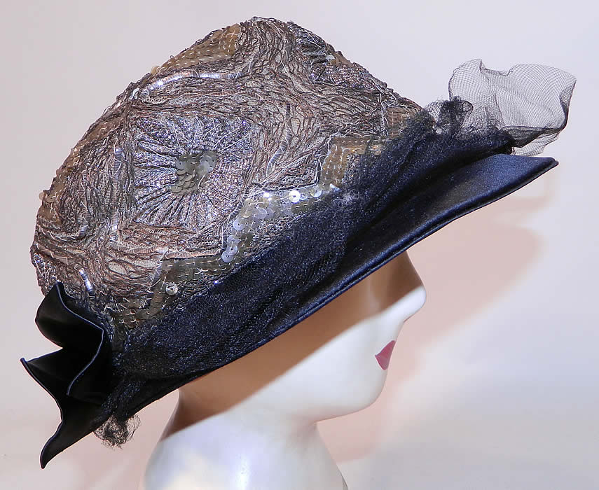 Vintage Emmaline Silver Lame Lam&eacute; Embroidered Sequin Trim Black Silk Wide Brim Cloche Hat. The hat is made of black silk wide brim, with black tulle net covering it, a black satin bow trim on back and silver metallic lam&eacute; embroidery work, iridescent sequins sewn onto a net crown on top. 