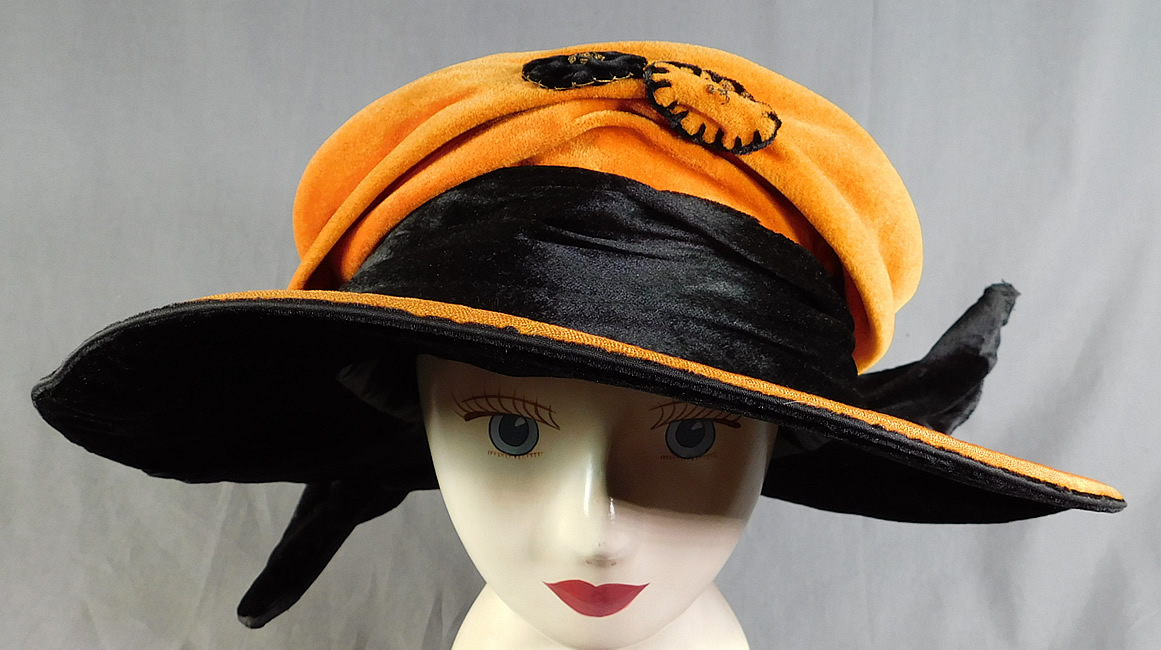 Vintage Harris Hat & Cloak Shop Orange Black Velvet Winged Wide Brim Cloche
The hat is made of a orange and black velvet fabric, with contrasting velvet rosette gold metallic embroidered applique trim on the front crown.