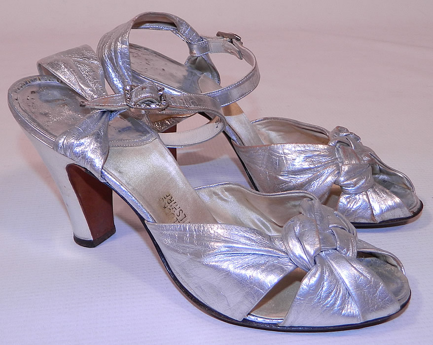 Vintage Bullock's Wilshire Silver Lamé Lame Leather Ankle Strap Evening Dance Shoes
These elegant evening dance shoes have a decorative knotted braided designs on the front instep vamps, with an open toe, adjustable ankle straps with rhinestone buckle closures and silver leather covered modified boulevard high heels.