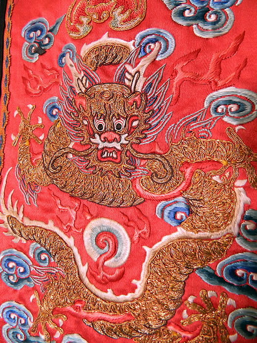Antique Chinese Chaoqun Court Apron Skirt Panel Embroidered Gold Dragon. There is a front facing gold "Long" five clawed dragon, with smoke clouds, flames, pearl, bat and waves of water along the bottom. The dragon symbolizes the emperor, who was regarded as the Son of Heaven. There is a black silk trim border edging with blue and white embroidered flowers, butterflies and a knotted fringe tassel trim hanging down from the bottom.