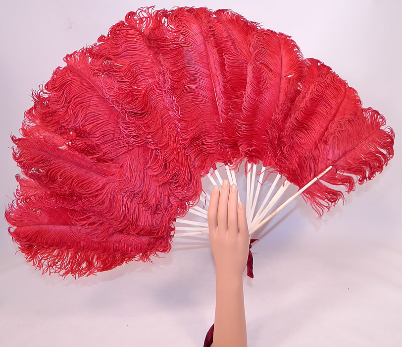 Antique Edwardian Red Ostrich Feather Folding Fan Velvet Ribbon
It is made of large fluffy dyed red ostrich feather plumes. There are bleached white bone sticks and guards with a loop, mother of pearl rivet and burgundy red silk velvet ribbon tie on the bottom for carrying.