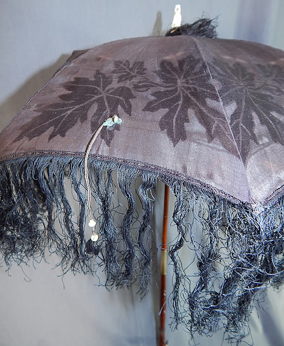 Victorian Antique Black Silk Damask Maple Leaf Carved Wood Folding Handle Parasol
This pretty parasol has a decorative carved turned wood folding shaft with sliding brass ring cap to hold in place, a fish hook style carved handle, bone finial ring top with fringe trim and attached strap to hold fabric closed. 